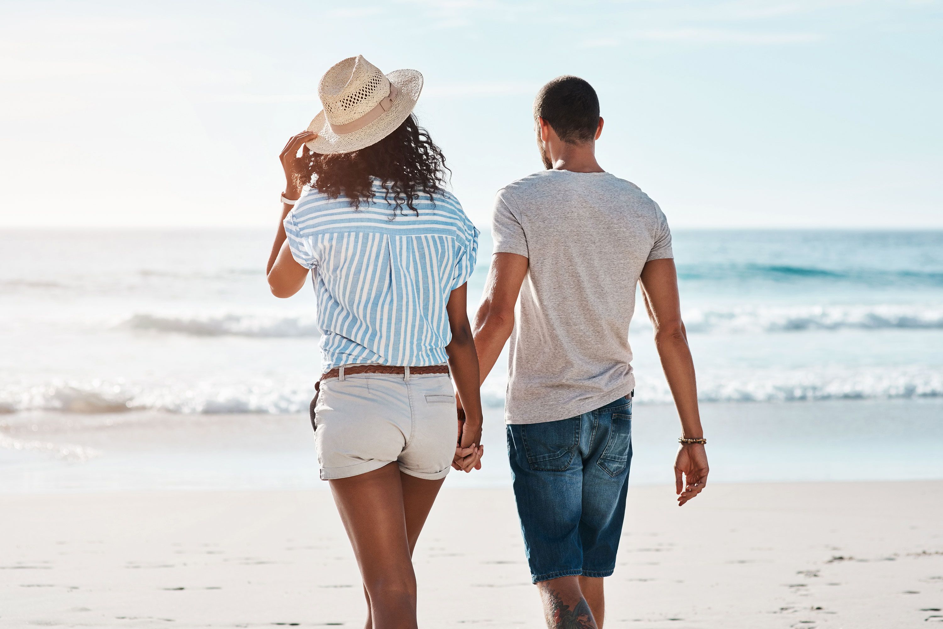 A young couple walking along the beach with their backs to the camera.