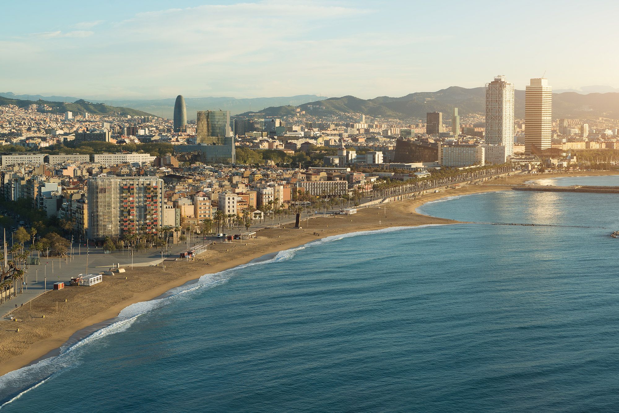 Aerial view of Barcelona Beach in the summer with the city skyline behind the Mediterranean Sea.