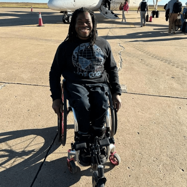 Ade Adepitan in his wheelchair on a runway, waiting to board a flight