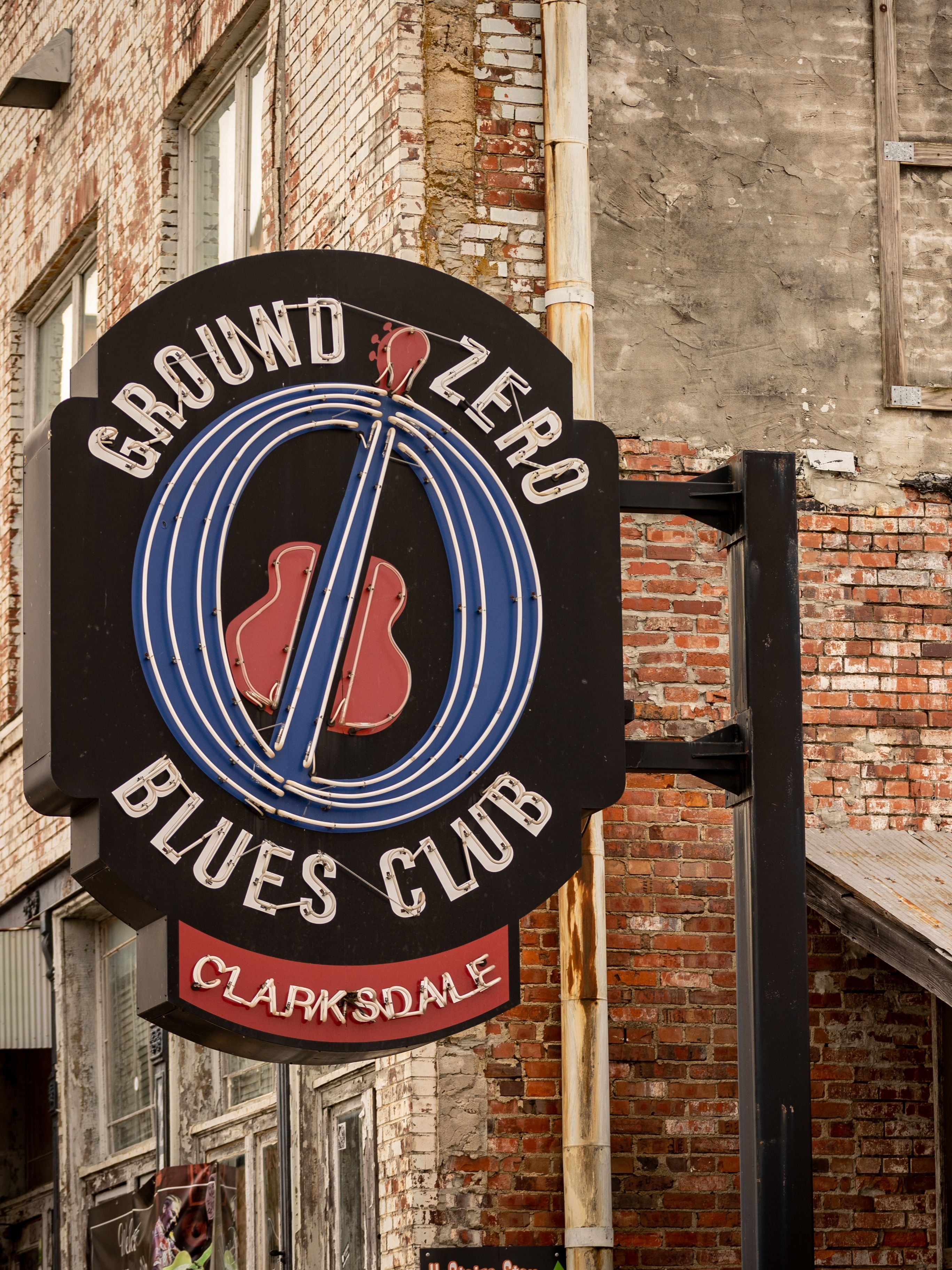 A sign for Ground Zero Blues Club with a guitar logo in Clarksdale Mississippi is attached to a red brick building