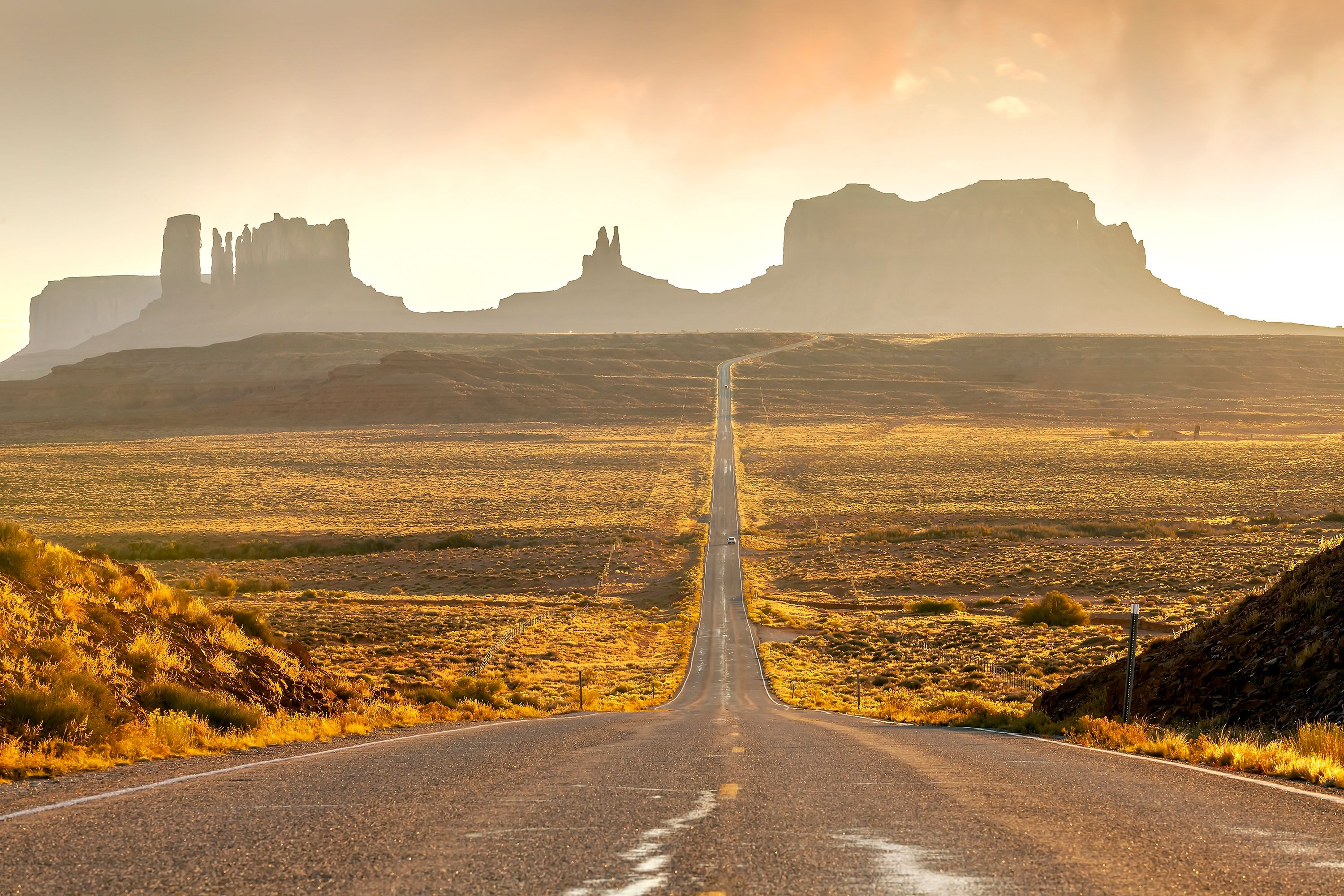 A long straight highway cutting through a desert like landscape towards rugged hills jutting out into the sky in the horizon.