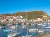 Sail boats in a harbor with buildings and a castle on a hill.