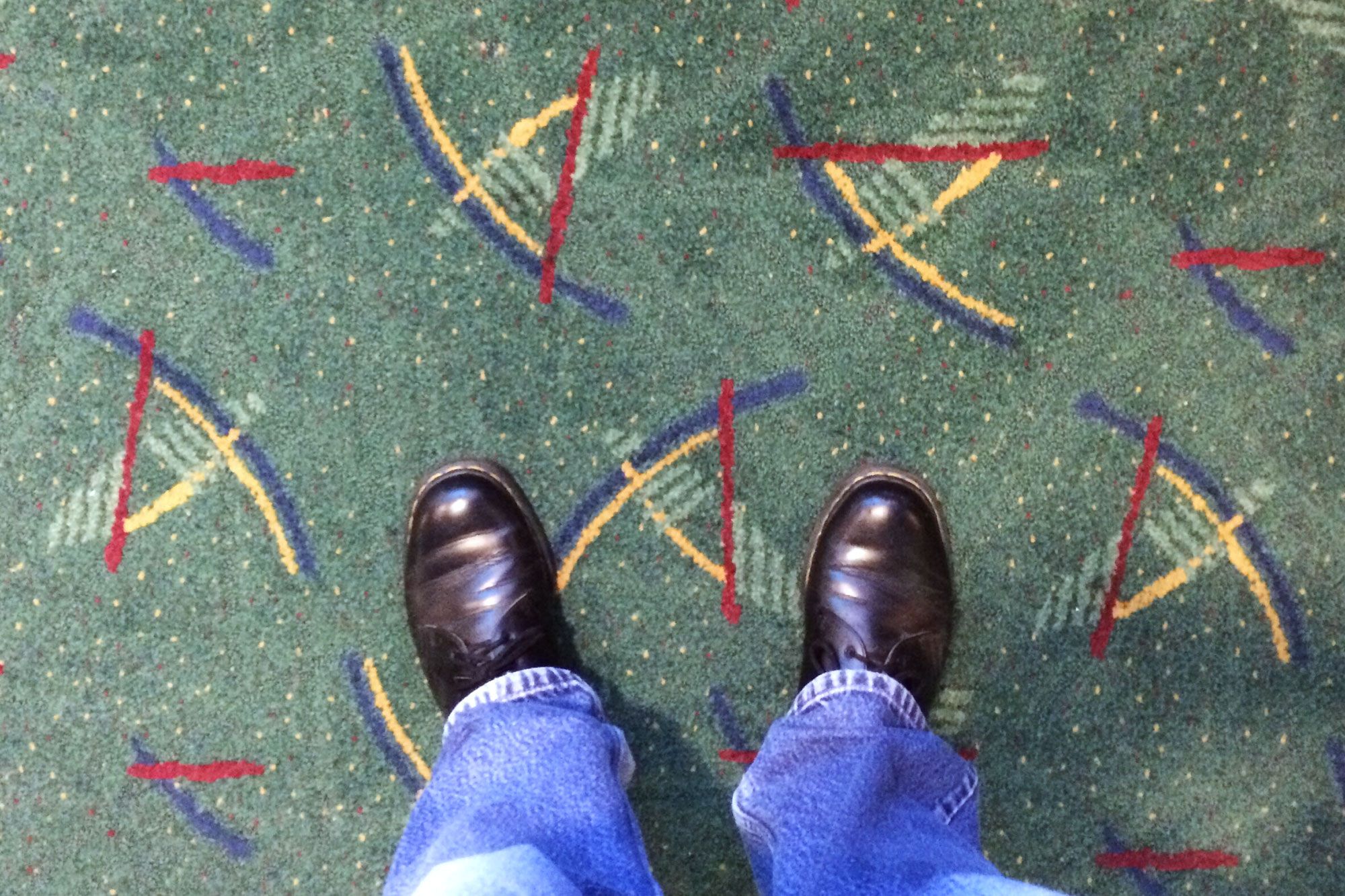 Feet standing on a green carpet with yellow, blue and red lines on it as decoration.