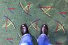 Feet standing on a green carpet with yellow, blue and red lines on it as decoration.