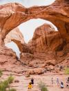 A giant formation of pink rock arches overhead, as a crowd of people walk beneath it