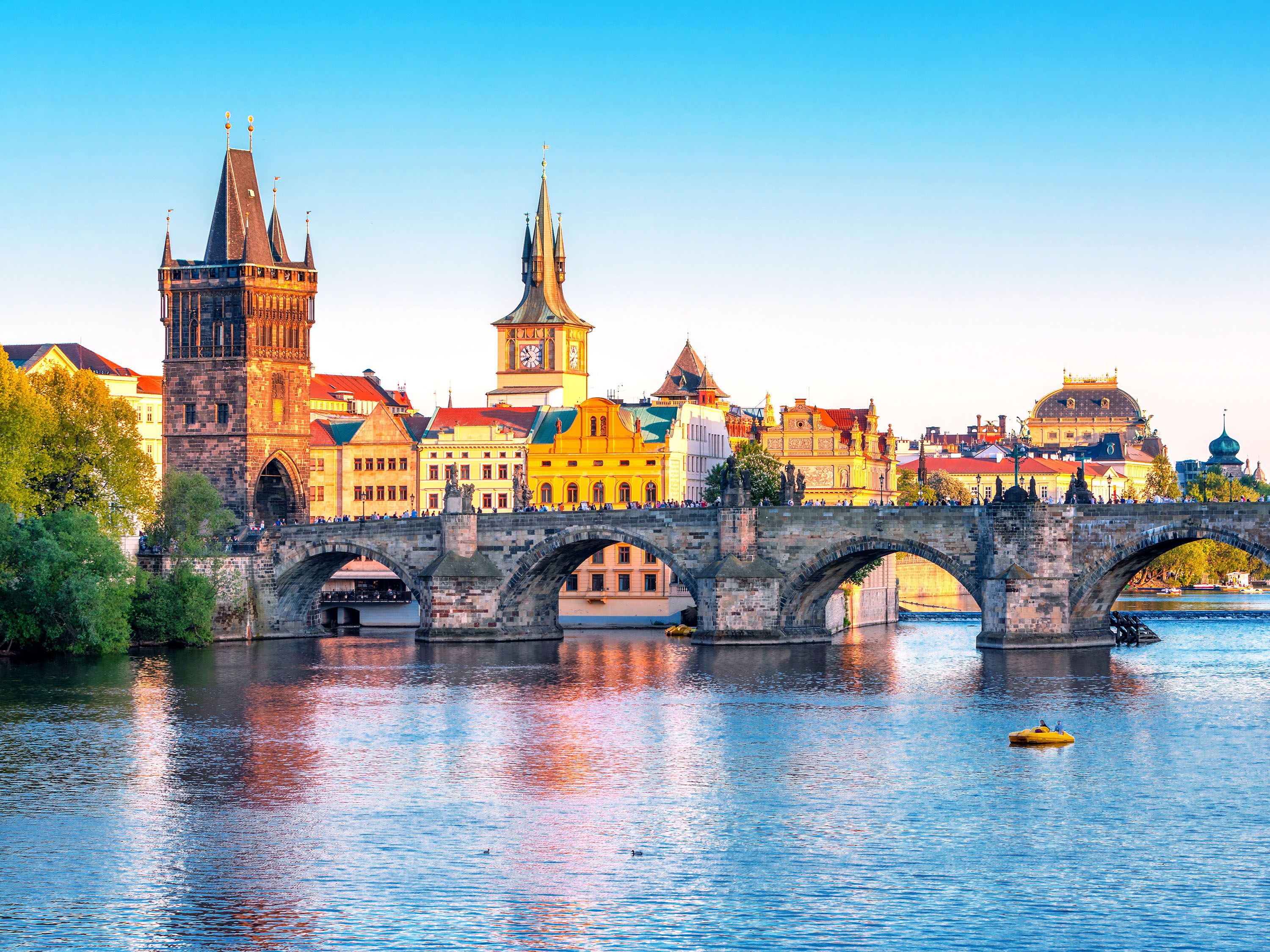 Stone bridge with a clocktower and city buildings at sunset.