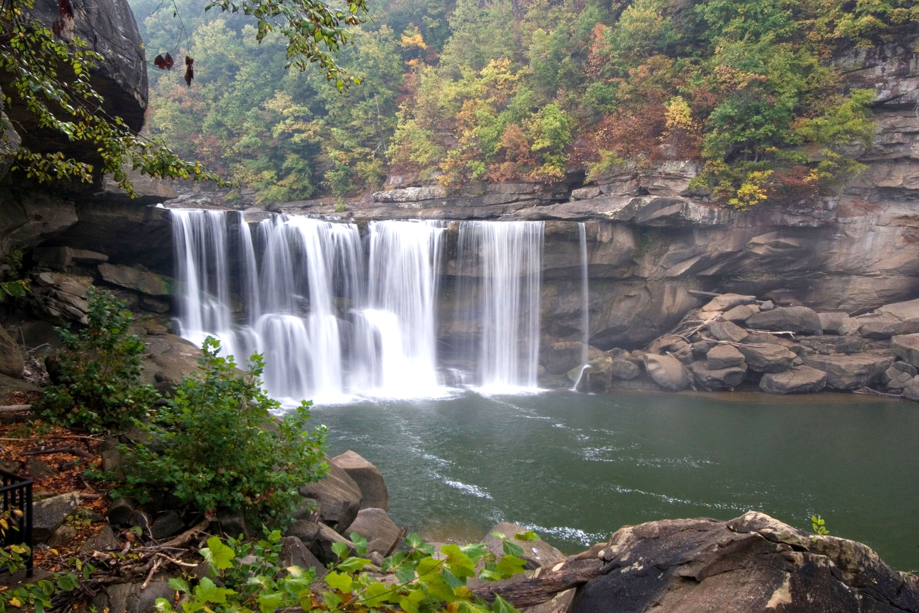 A waterfall cascading into a rocky pool, surrounded by green trees.