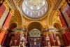 An interior view of St. Stephen’s Basilica in Budapest showing the basilica’s domed ceiling with decorative mosaics, tall marble columns, and richly ornamented arches, bathed in soft natural light.
