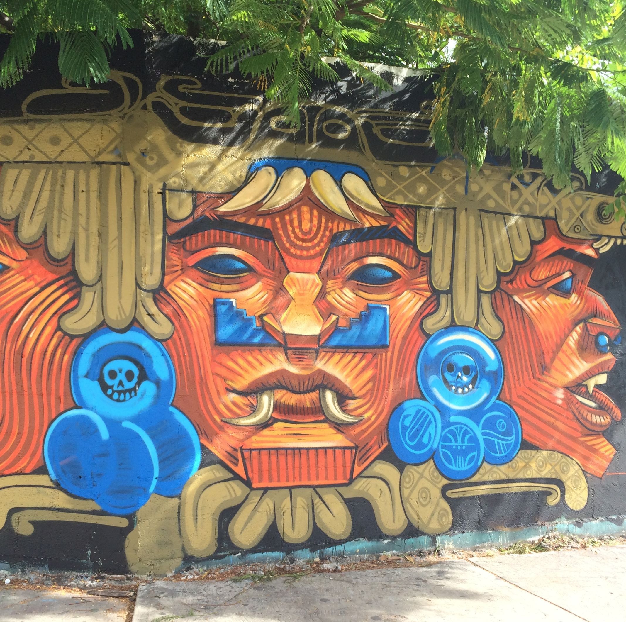 A colorful mural featuring warrior faces by Apitatán. (Image courtesy of meetingofstyles.com)