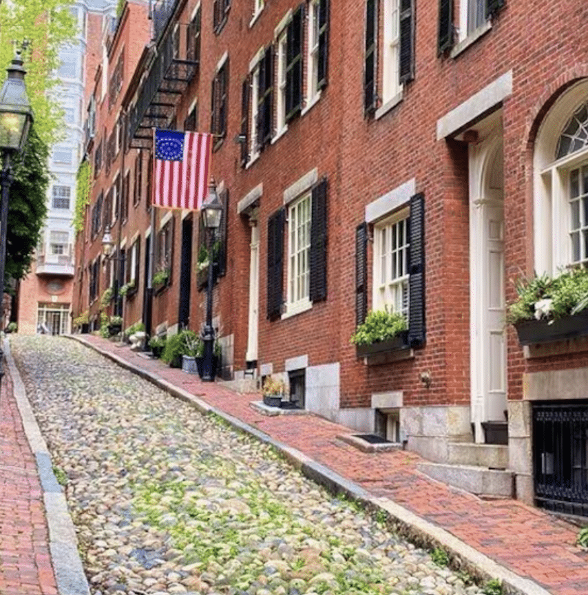 Red-brick buildings with shuttered windows line a cobbled street in Boston, Massachussets