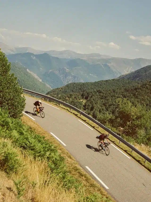 Two cyclists head downhill on a mountainous road in the countryside