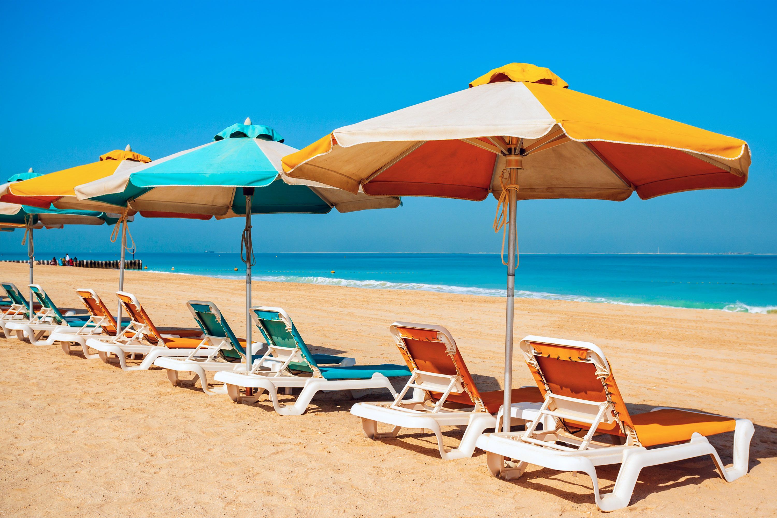 Rows of multicolored beach umbrellas set up in the sand at Kite Public Beach. in Dubai, with the sea and sky in the background.