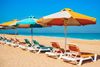Rows of multicolored beach umbrellas set up in the sand at Kite Public Beach. in Dubai, with the sea and sky in the background.