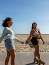 Two women rollerskate in the sunshine beside a beach in Los Angeles, California