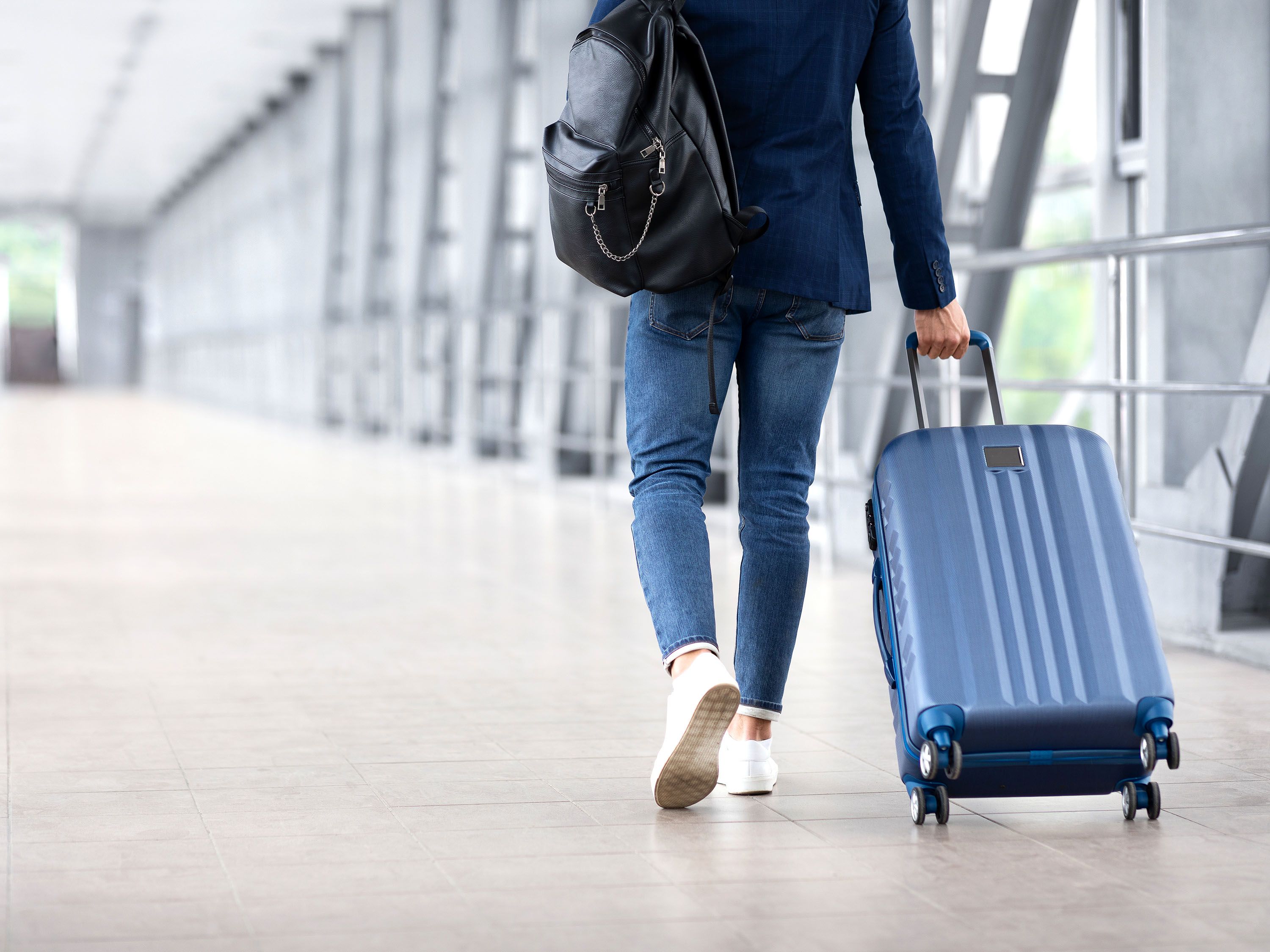 A person walks through an airport with roller bag pulled behind.