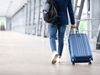 A person walks through an airport with roller bag pulled behind.