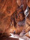 A man walks through the middle of vast curved red rocks in Paria Canyon