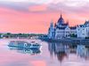 View of the Hungarian Parliament building under a pink sunset sky with a cruise ship on the Danube River in Budapest, Hungary.