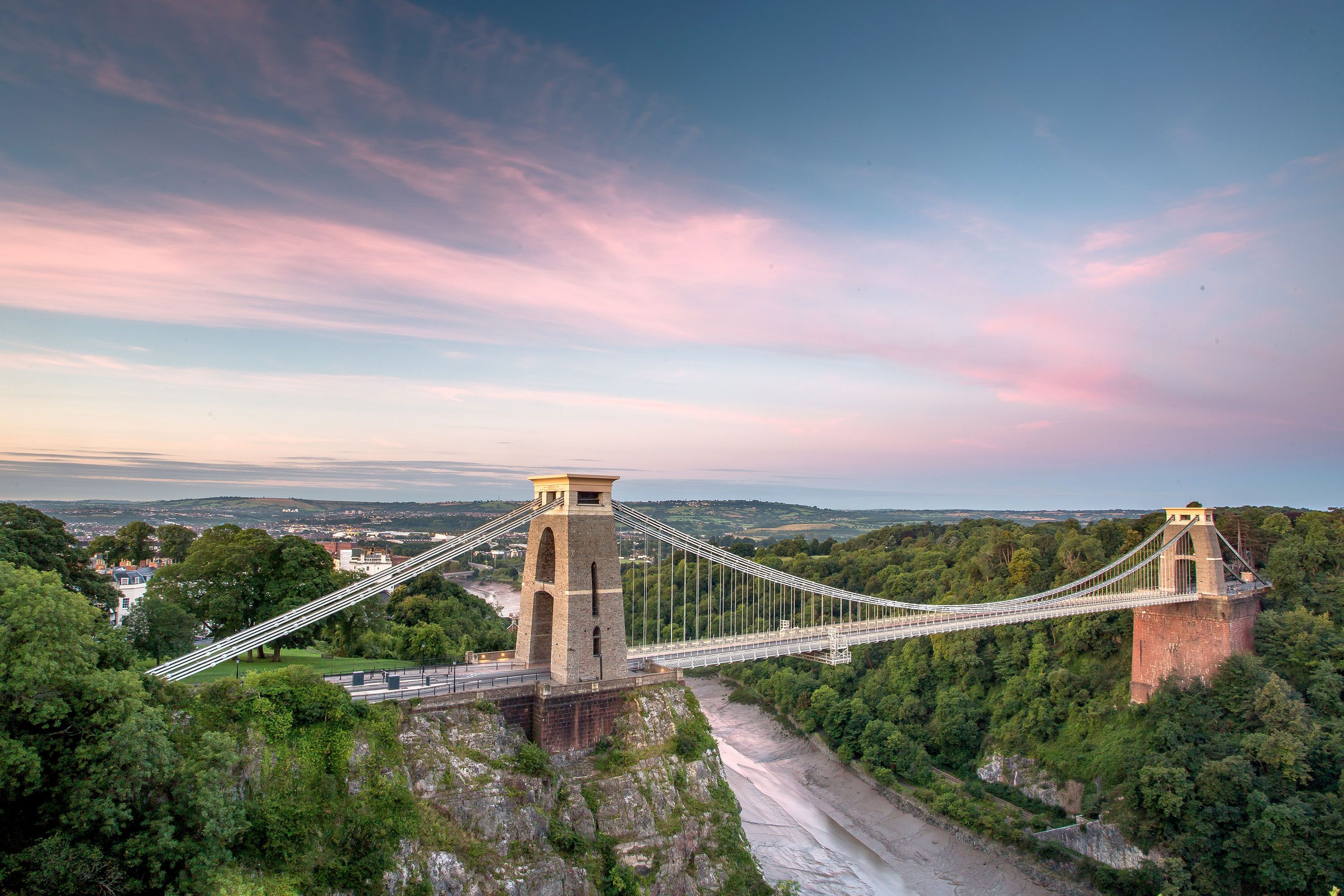 View of suspension bridge over water with pink sky.