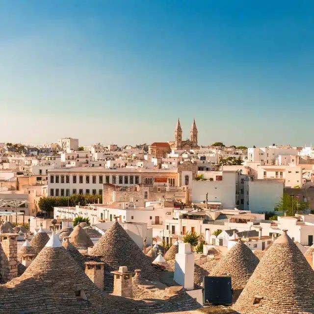 The traditional trulli, or stone huts with coned roofs, are visible in the foreground of the town of Alberobello in Apulia, Italy