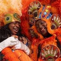Spy Boy Honey and Queen Ausettua of the Mardi Gras Indians laugh together in colorful suits and headdresses