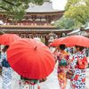 Women in colourful kimonos holding red umbrellas approach Dazaifu Tenmangu Shrine in Fukuoka, Japan