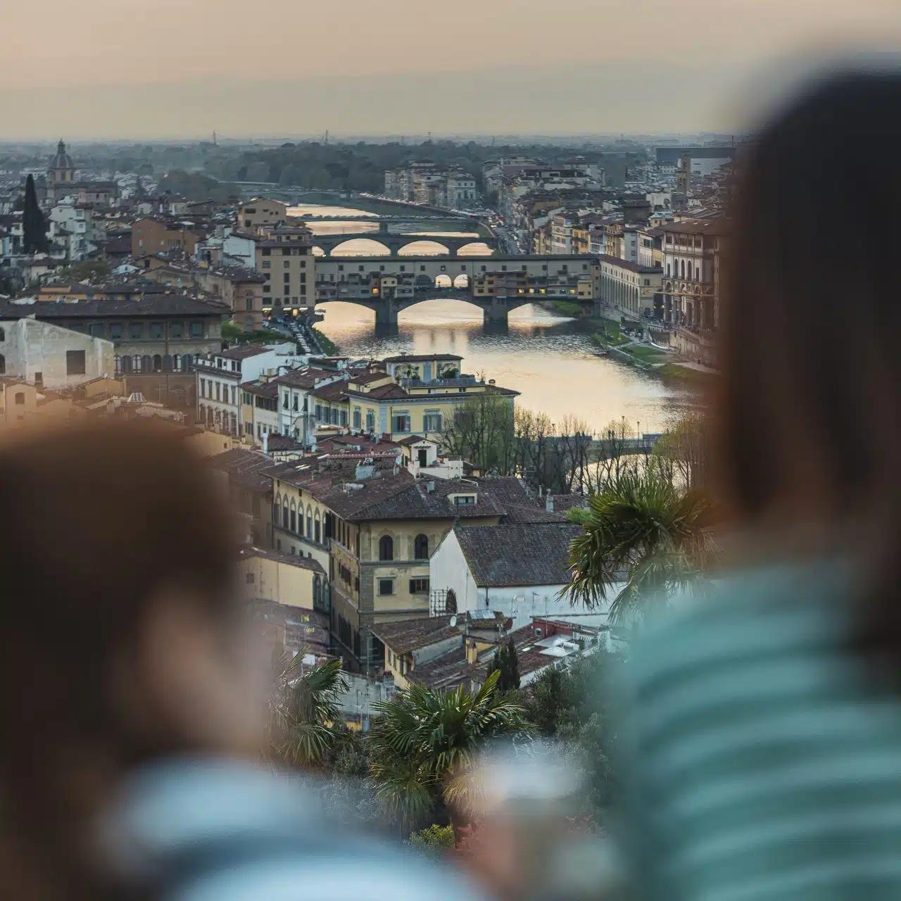Two people seen blurred from behind look out to Ponte Vecchio from Piazzale Michelangelo in Florence, Italy