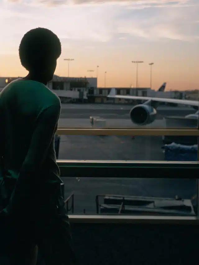 A person looks over a balcony at an airplane parked at a gate, at sunset
