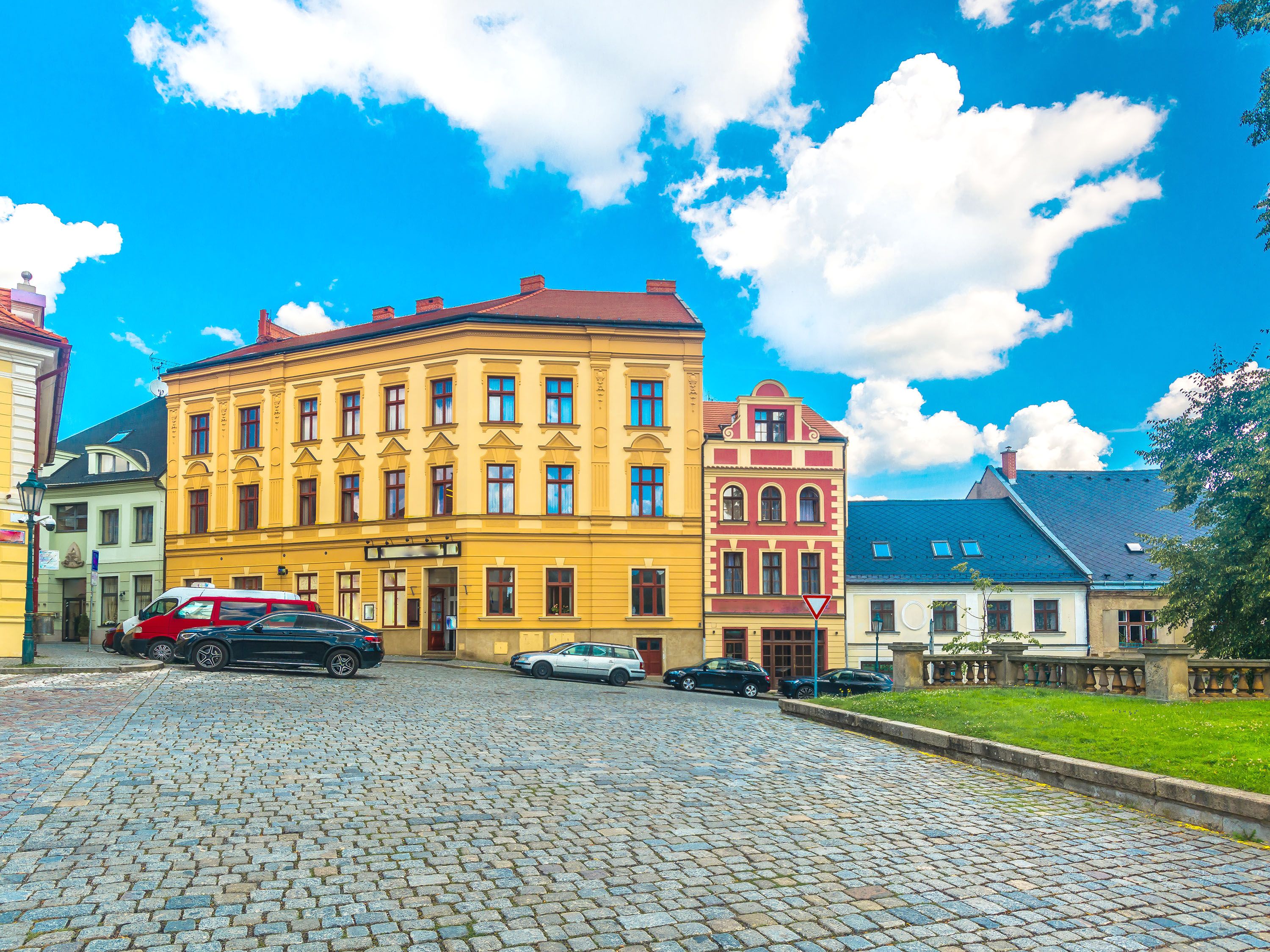 Cobblestone street with cars parked in front of a large yellow building.