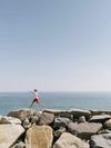 A child jumps along giant rocks with the sea beyond
