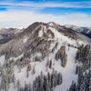 A snow-covered mountain scattered with tall trees beneath blue skies