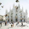 Milan's gothic Duomo in hazy summer sunlight, with a flock of pigeons taking off