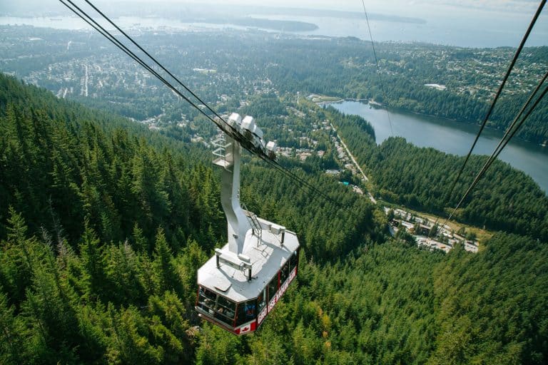 A cable car zips up the steep incline of Grouse Mountain with a blanket of evergreens covering the slope below