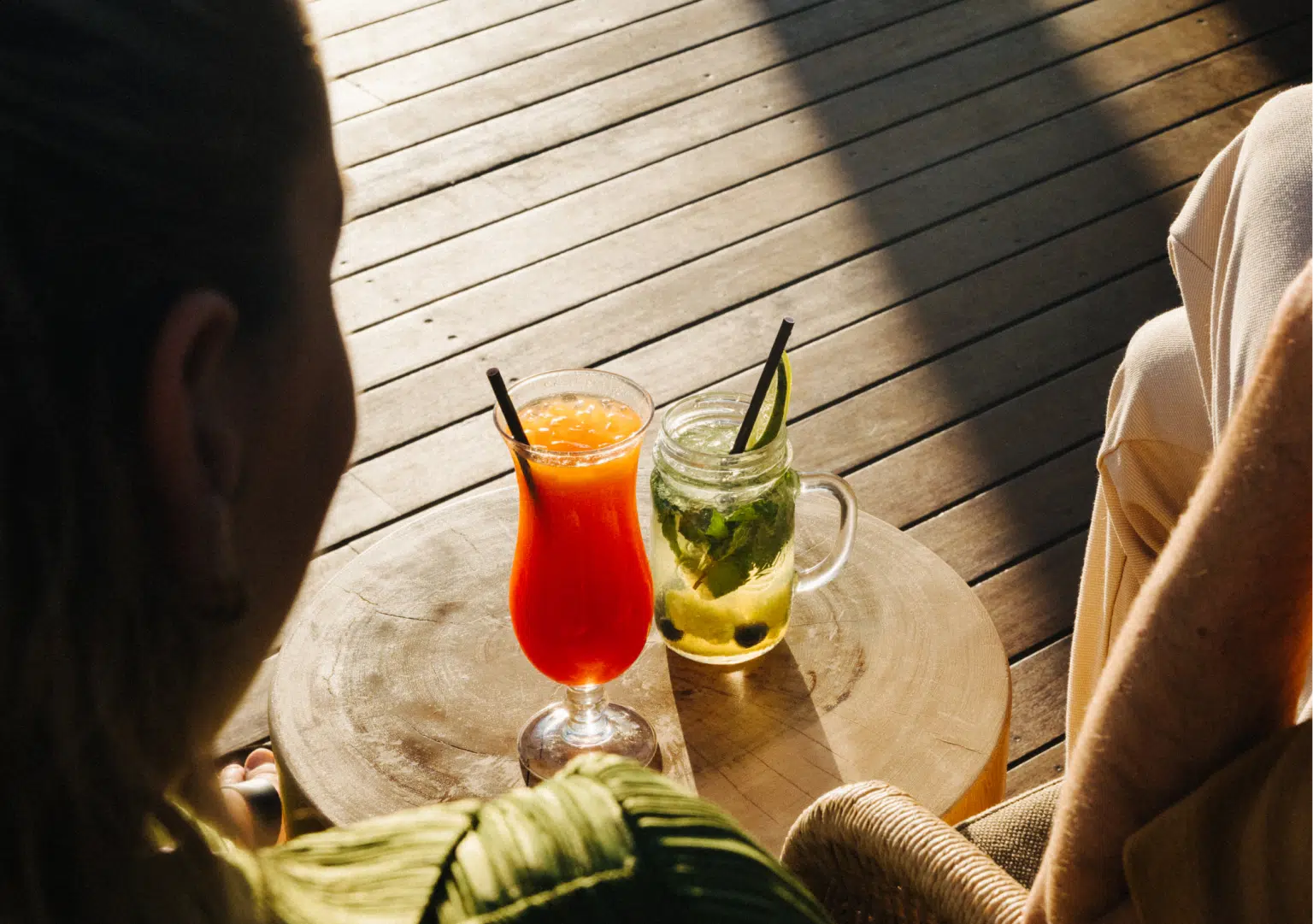 Two people seen from behind sit at a table holding two cocktail-style drinks