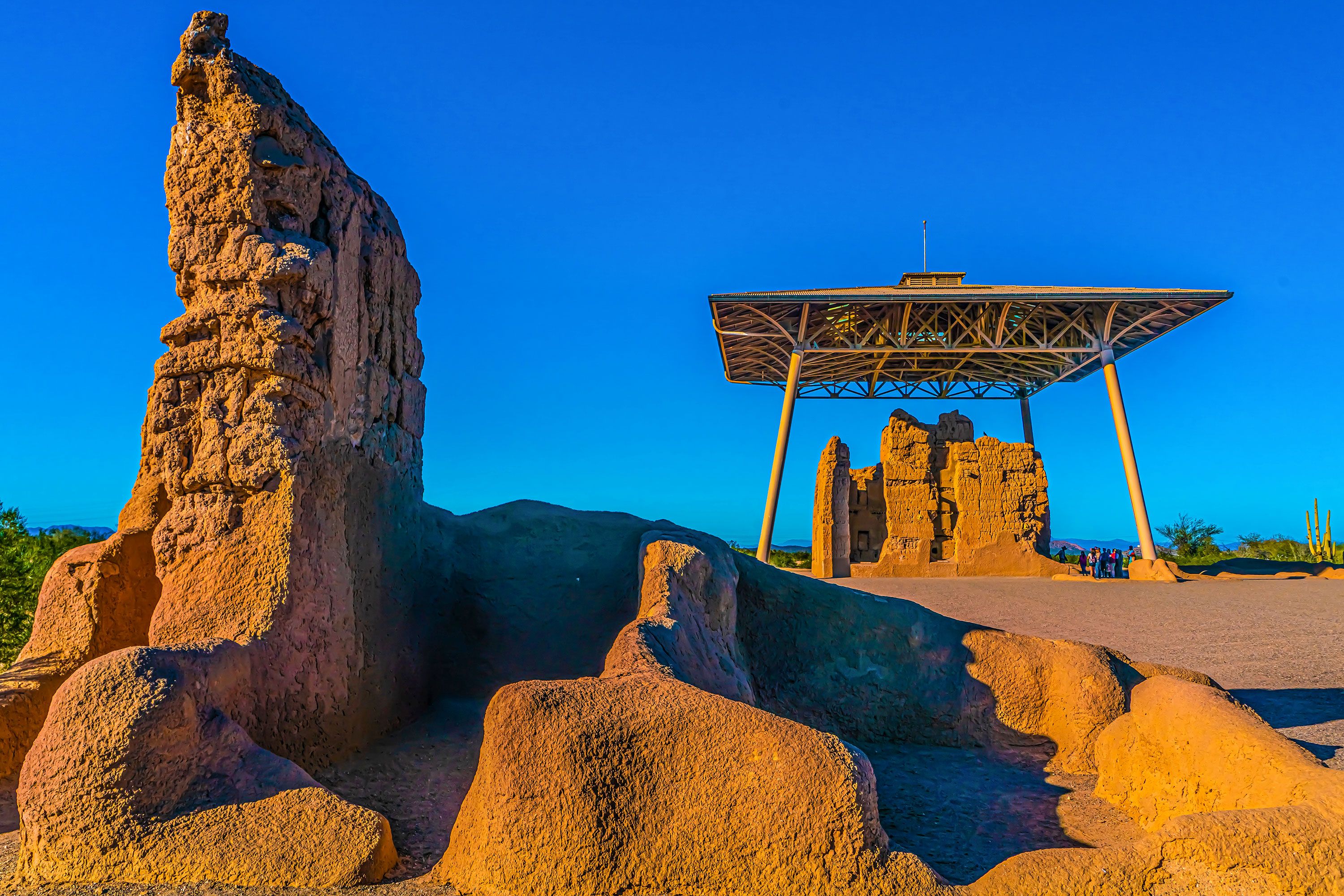 Weathered red stone structures with some under a protective wooden cover  under a blue cloudless sky.