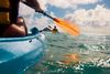 Two people in blue kayaks paddle out on the sea on a bright, partly cloudy day