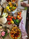 Overflowing bowls of tomatoes, lemons and limes share a busy kitchen table with fruit, as a person chops veg
