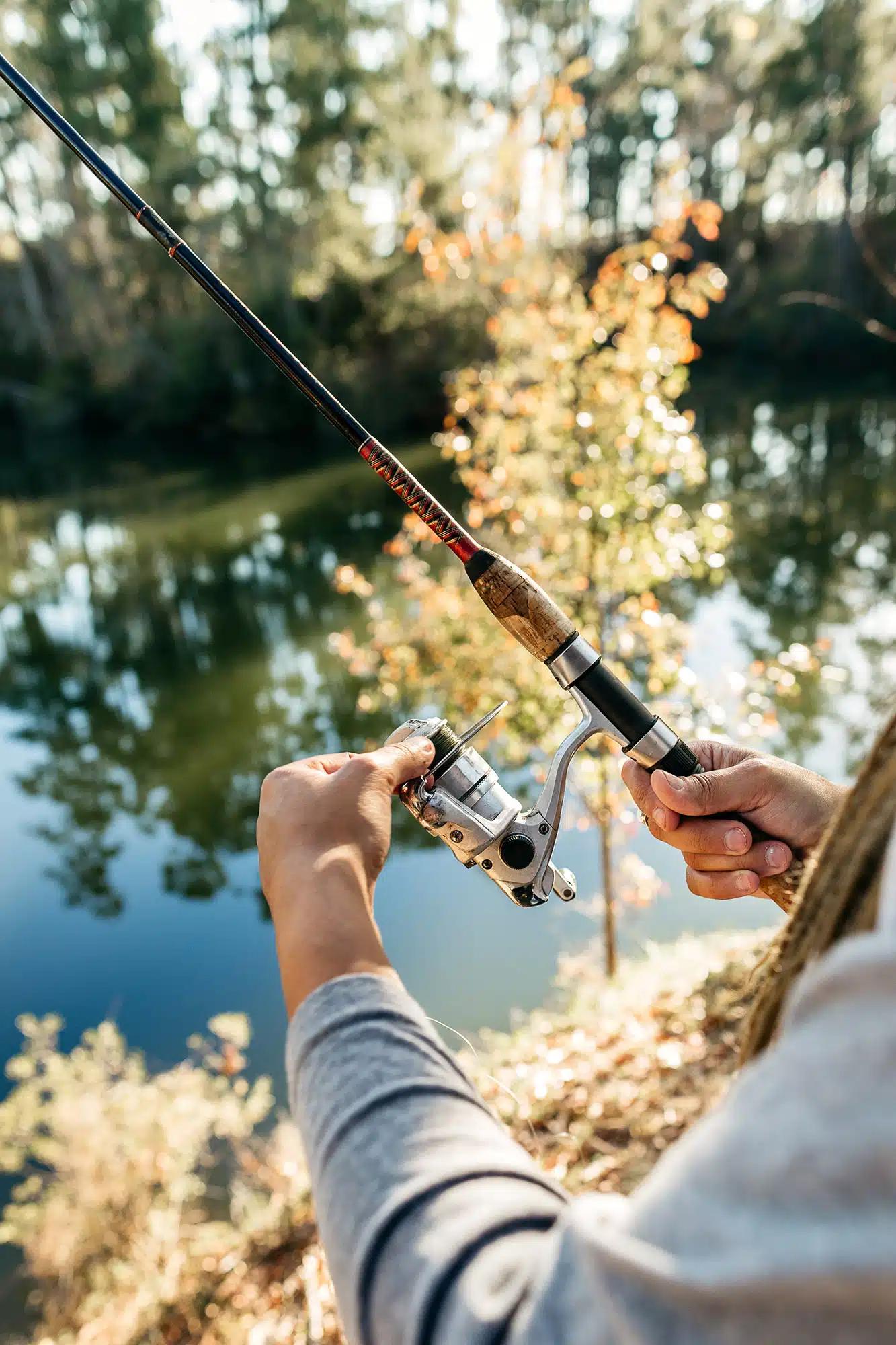 A close up of a person with a fishing rod beside a river