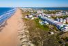 An expansive sandy shore, gentle Atlantic surf, and a bright, clear sky, evoking a peaceful seaside escape.
