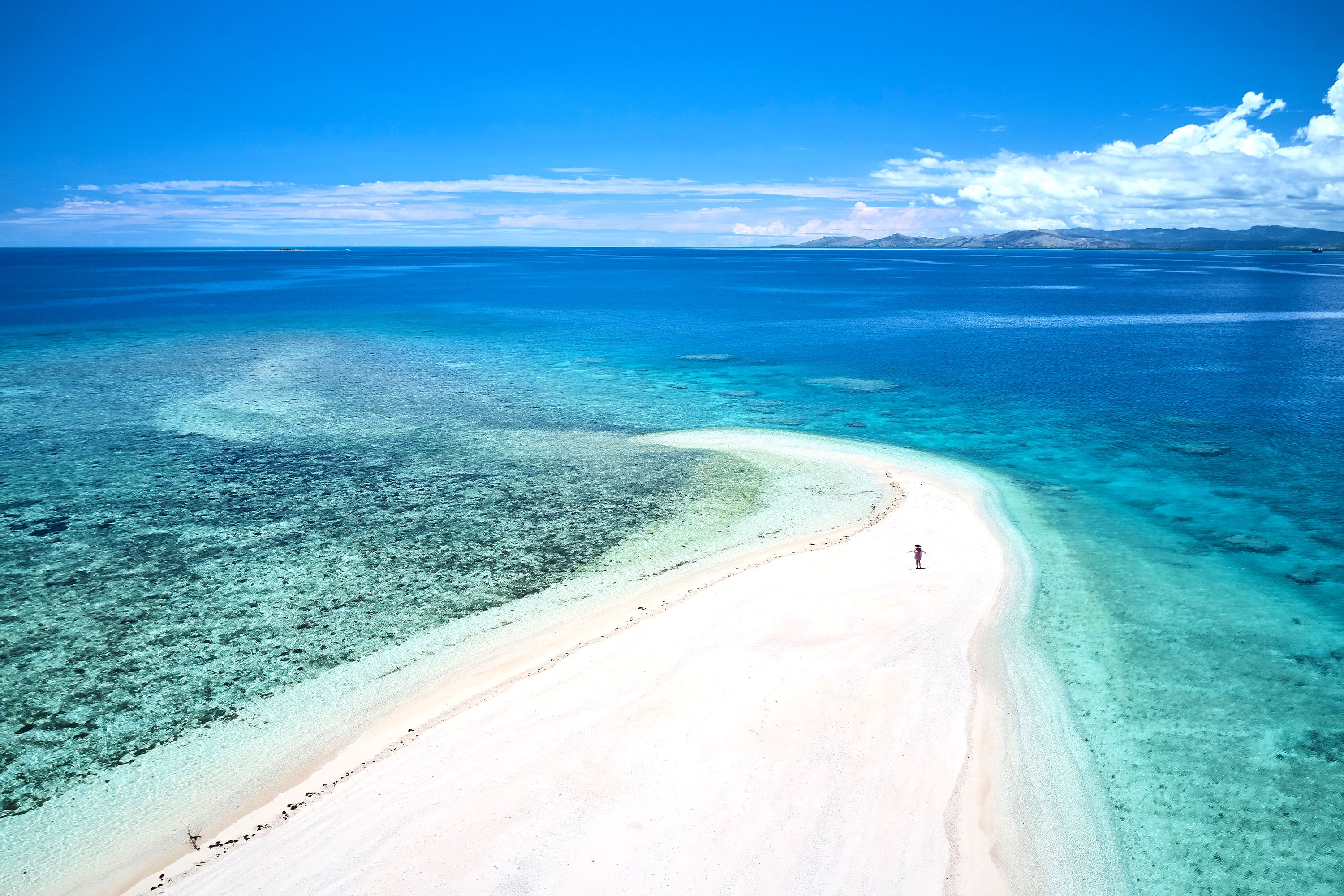 An aerial view of a small piece of land with white-sand in the middle of turquoise waters.