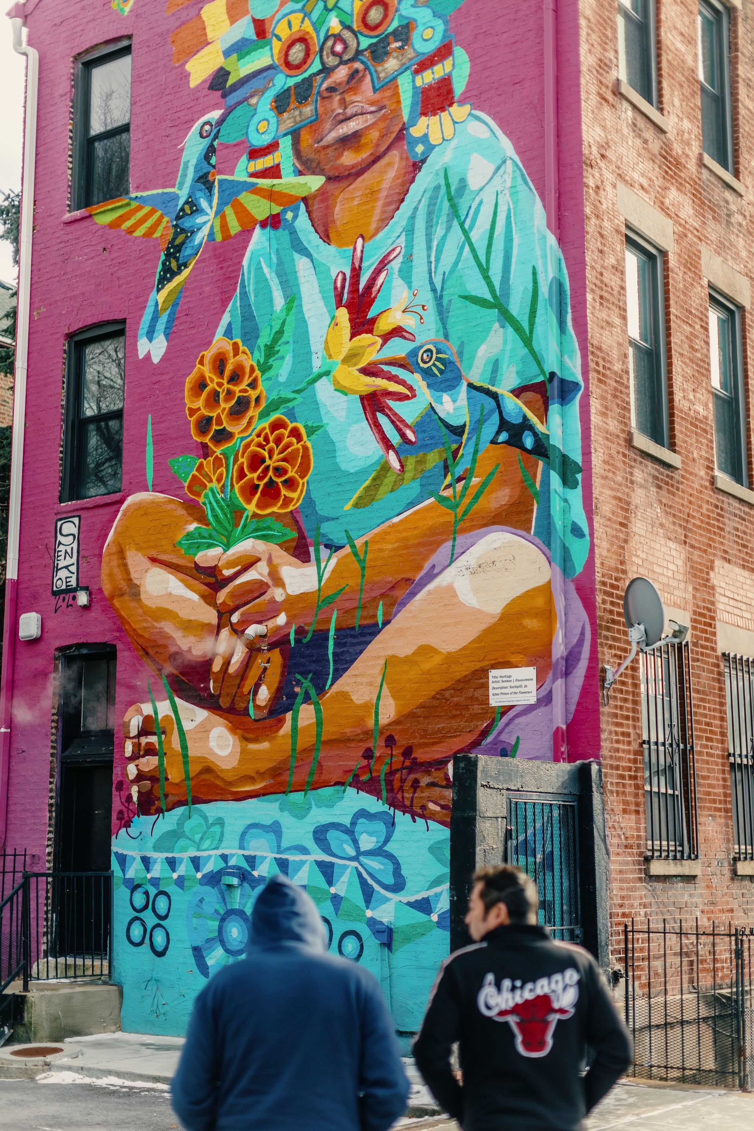 A large, colorful mural adorns the side of a multi-storey building in Pilsen, Chicago