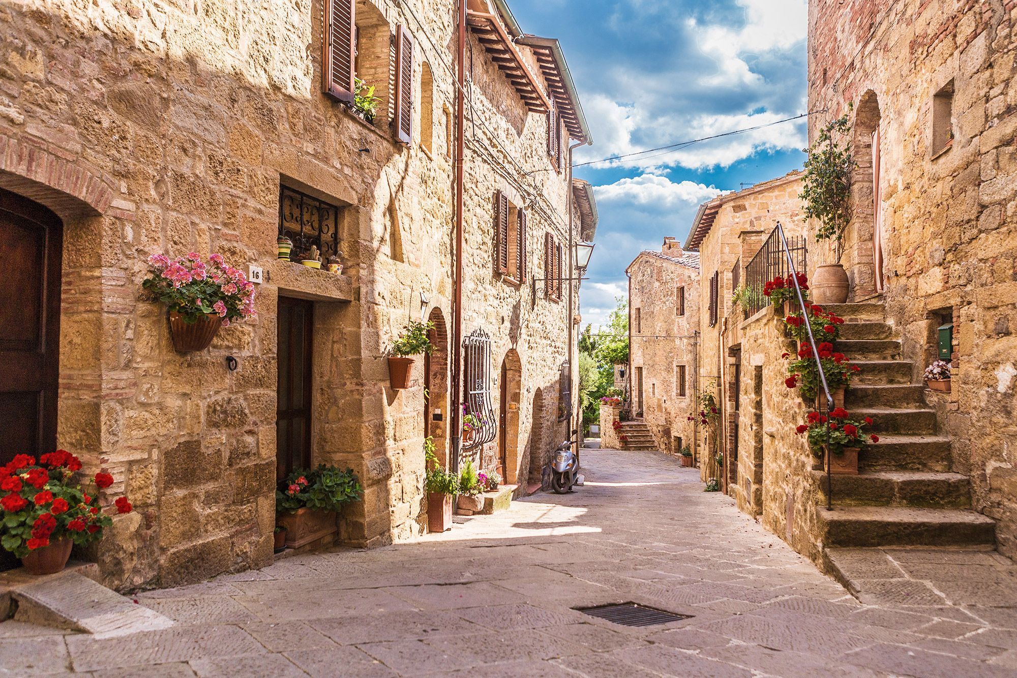 A street lined with stone buildings and flowers on the walls in the town of Pienza, Italy.