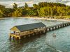 Ariel view from the water of people on the covered Hanalei pier and a person on a paddle board in the bay at sunset.