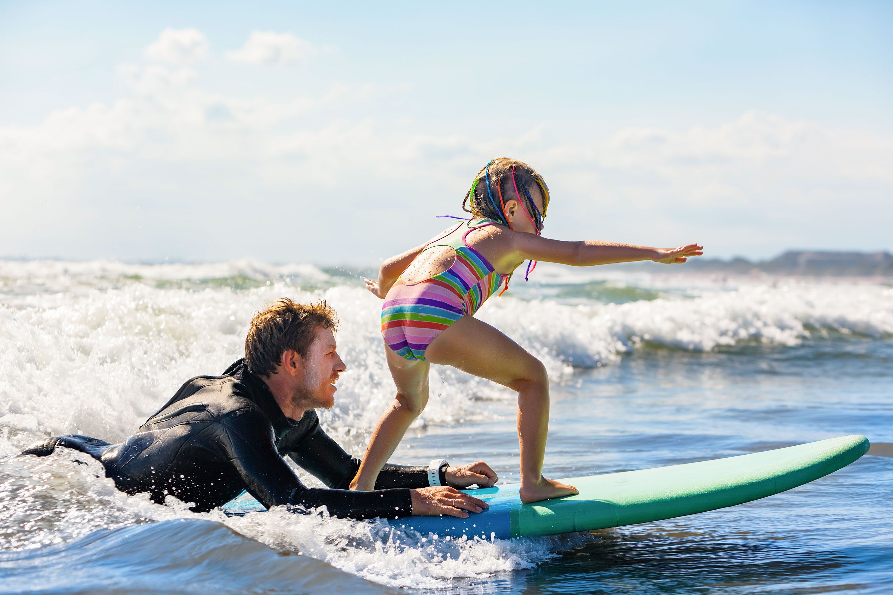 Little girl surfs while instructor in wet suit hangs on back of board.
