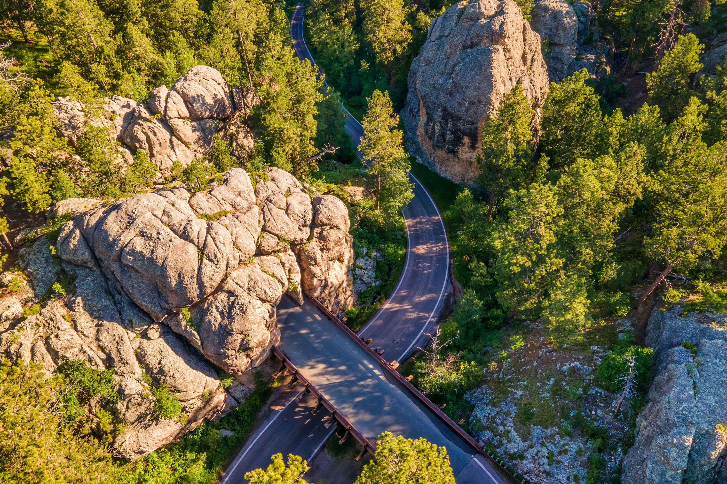 A  road curves between towering rock cut formations and dense green forest.