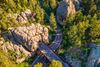 A road curves between towering rock cut formations and dense green forest.