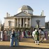 An exterior view of Chiswick House in West London, with people dressed in Regency-era costume in the grounds, in a scene from Bridgerton