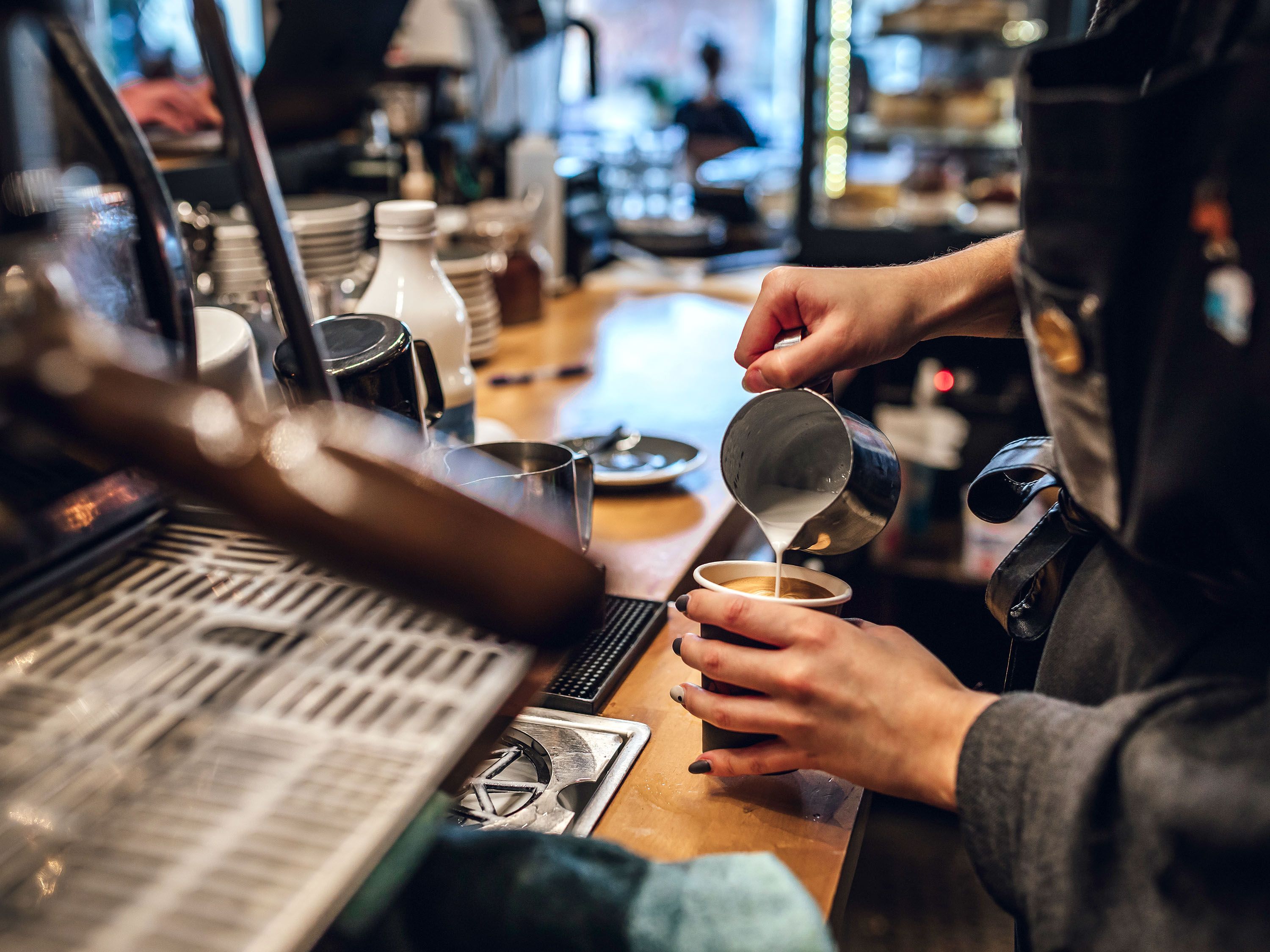 A barista pours steamed milk onto a coffee drink.