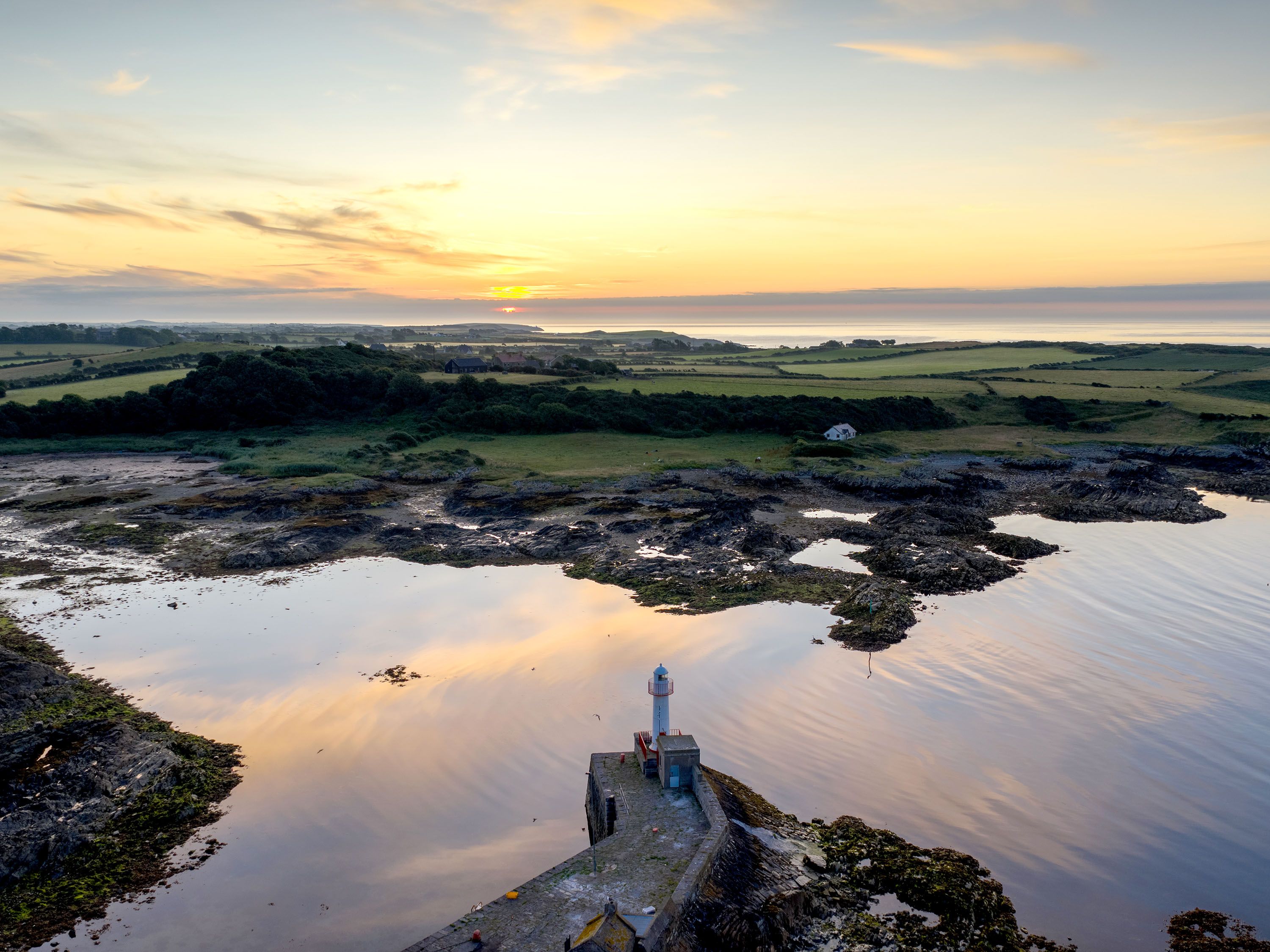 Sun setting on marshy land with a lighthouse.