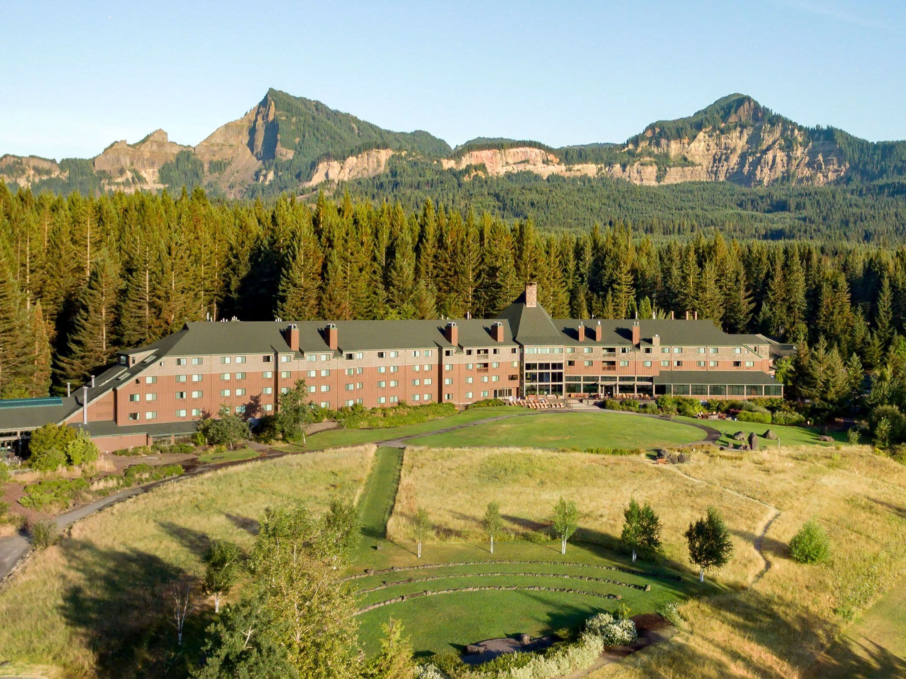 A mountain lodge surrounded by forest with rugged peaks rising behind.